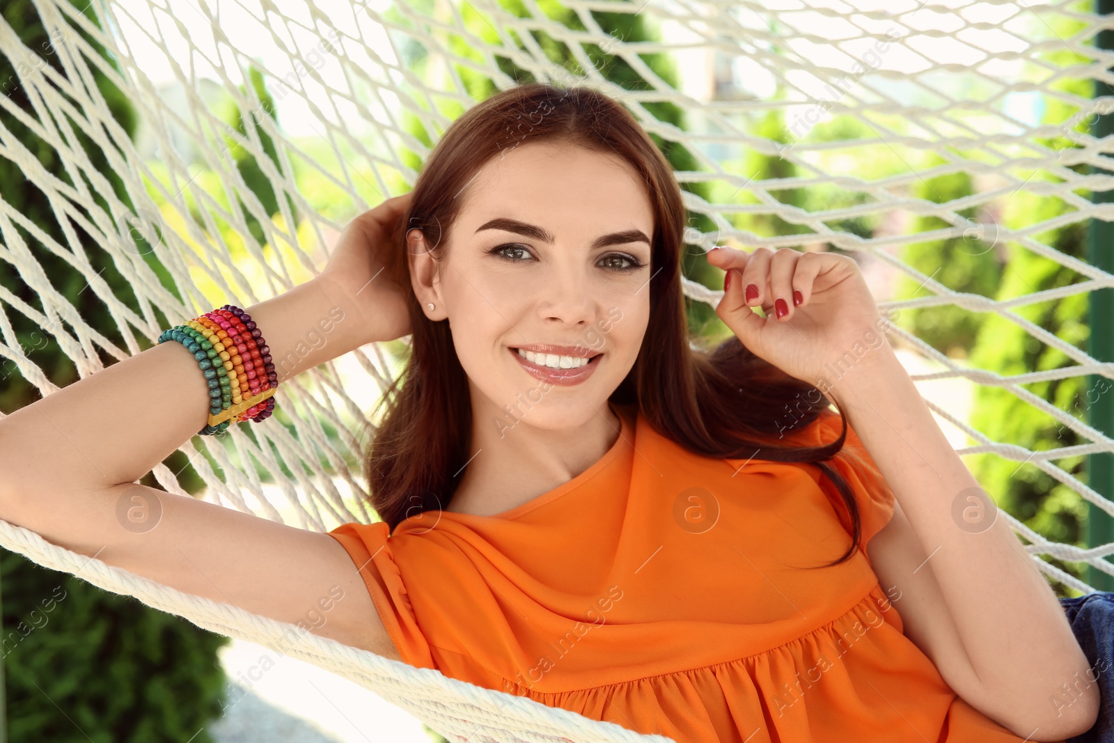 Photo of Young woman relaxing in hammock outdoors on warm summer day