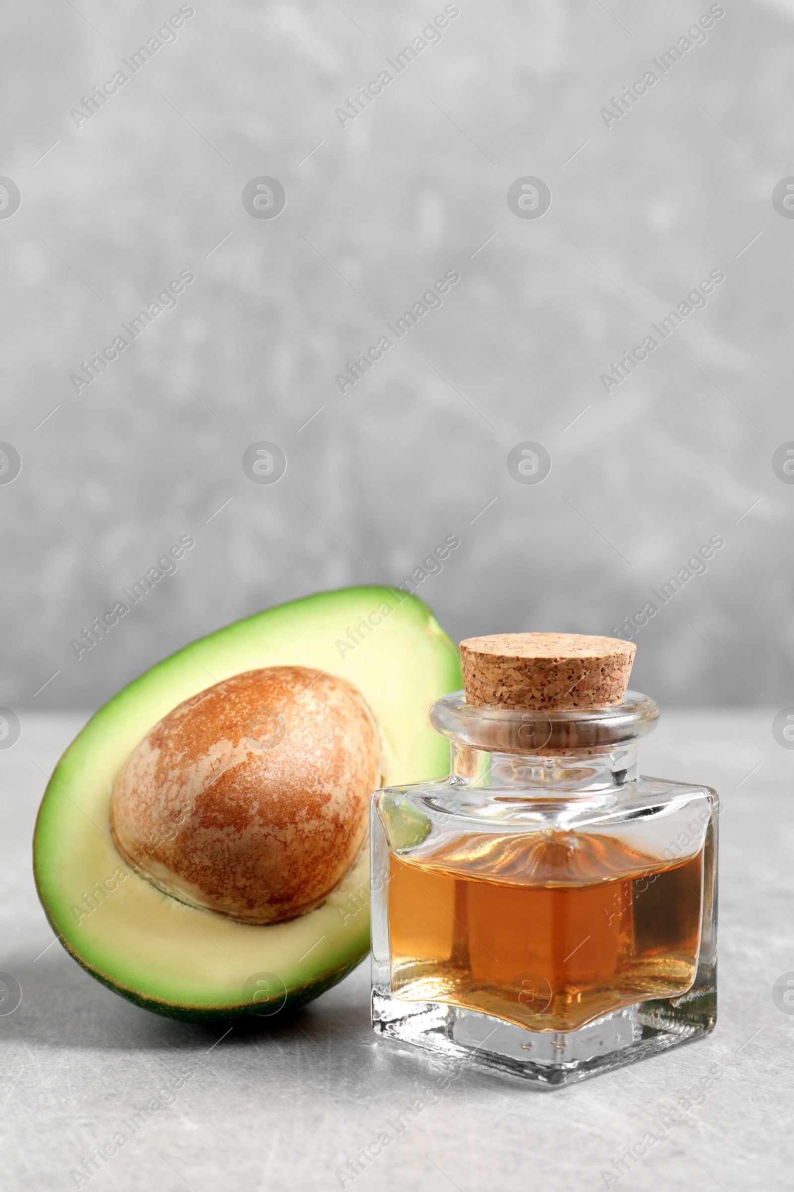 Photo of Bottle of essential oil and fresh avocado on grey table, space for text