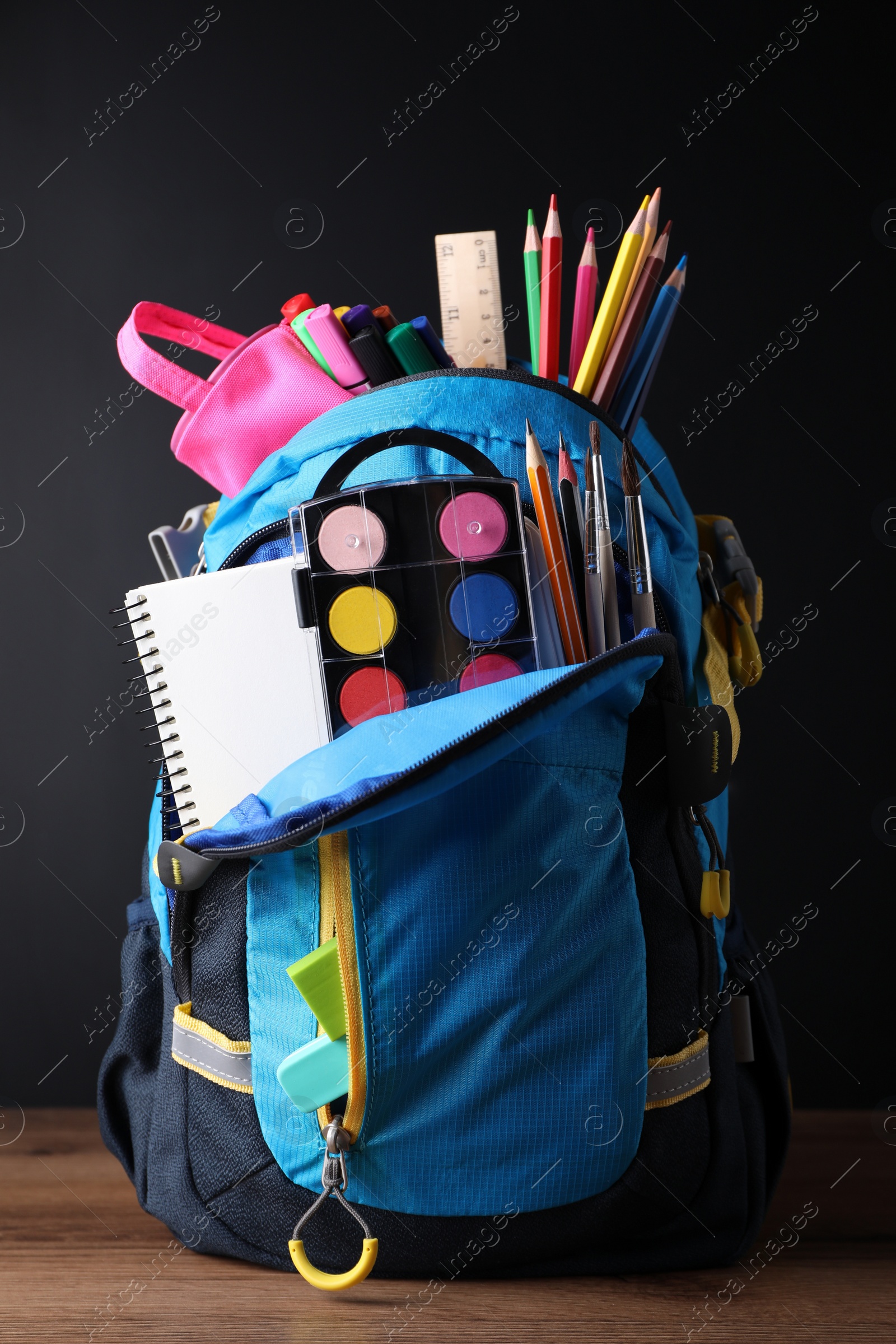 Photo of Backpack with different school stationery on wooden table near blackboard