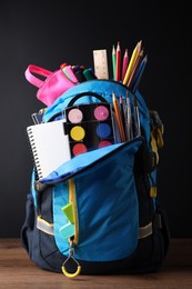 Photo of Backpack with different school stationery on wooden table near blackboard