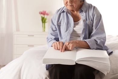 Blind senior person reading book written in Braille on bed indoors, closeup. Space for text