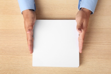 Photo of Man holding blank paper sheets for brochure at wooden table, top view. Mock up