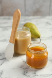 Photo of Tasty baby food in jars, pear and spoon on white marble table