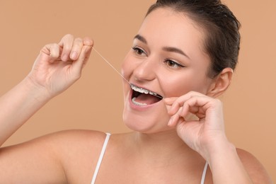 Photo of Woman with braces cleaning teeth using dental floss on brown background