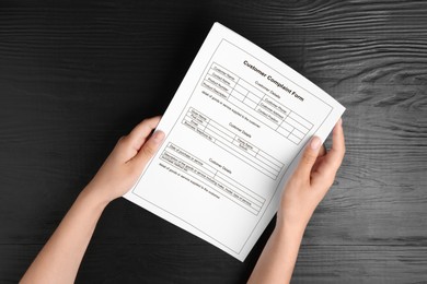 Image of Woman holding complaint form at black wooden table, top view