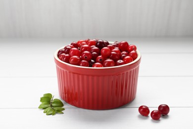 Fresh ripe cranberries in bowl on white wooden table, closeup