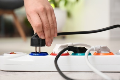 Photo of Woman inserting power plug into extension cord on floor indoors, closeup. Electrician's professional equipment