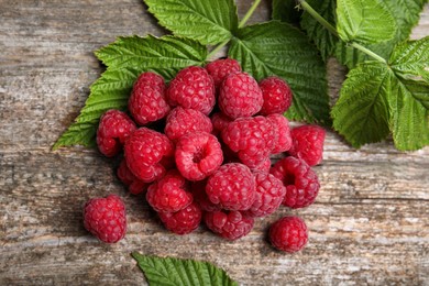 Photo of Fresh ripe raspberries and green leaves on wooden table, flat lay