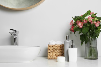 Photo of Vase with beautiful Alstroemeria flowers and toiletries near sink in bathroom