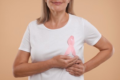 Photo of Breast cancer awareness. Woman with pink ribbon doing self-examination on light brown background, closeup