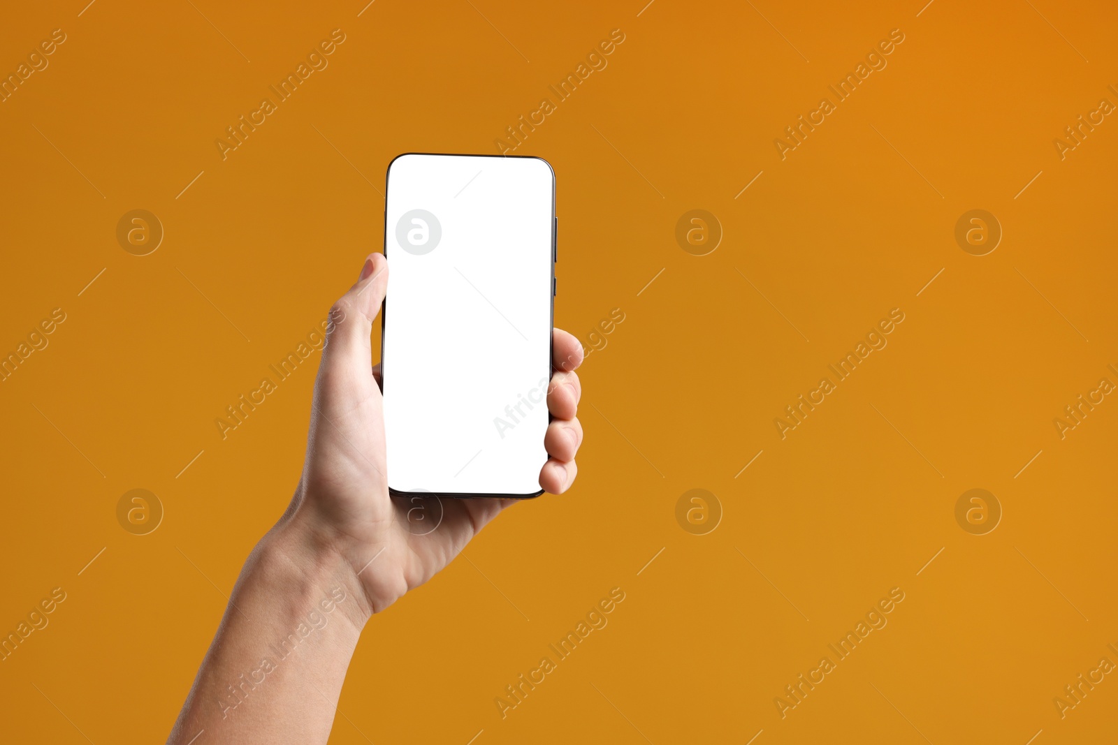 Photo of Man holding smartphone with blank screen on orange background, closeup. Mockup for design