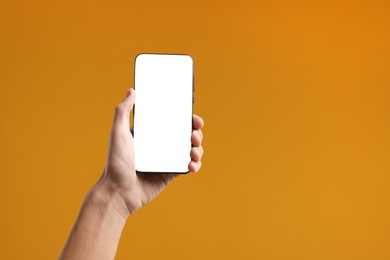 Photo of Man holding smartphone with blank screen on orange background, closeup. Mockup for design