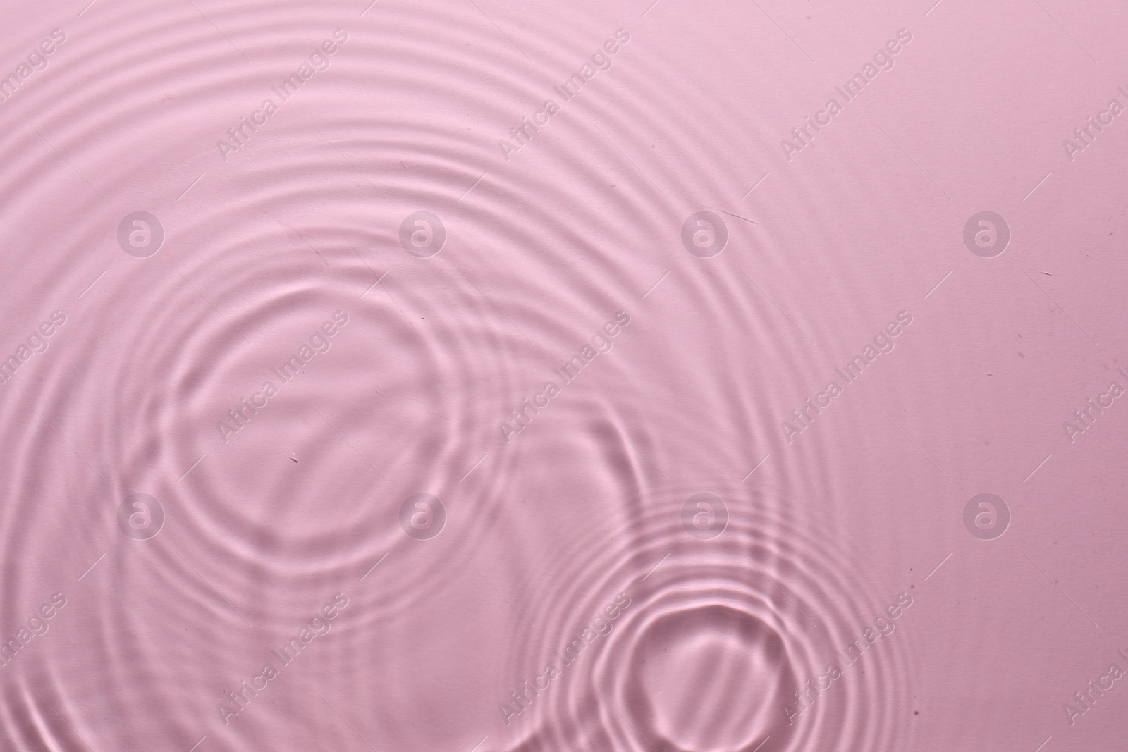 Photo of Rippled surface of clear water on pink background, top view