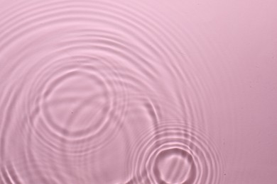 Photo of Rippled surface of clear water on pink background, top view