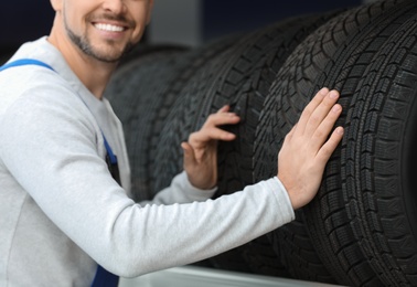 Photo of Mechanic near rack with car tires at service station, closeup