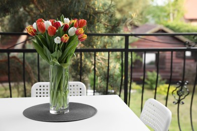Photo of Beautiful colorful tulips in glass vase on white table at balcony, space for text