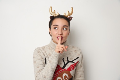 Photo of Young woman in Christmas sweater and deer headband on white background