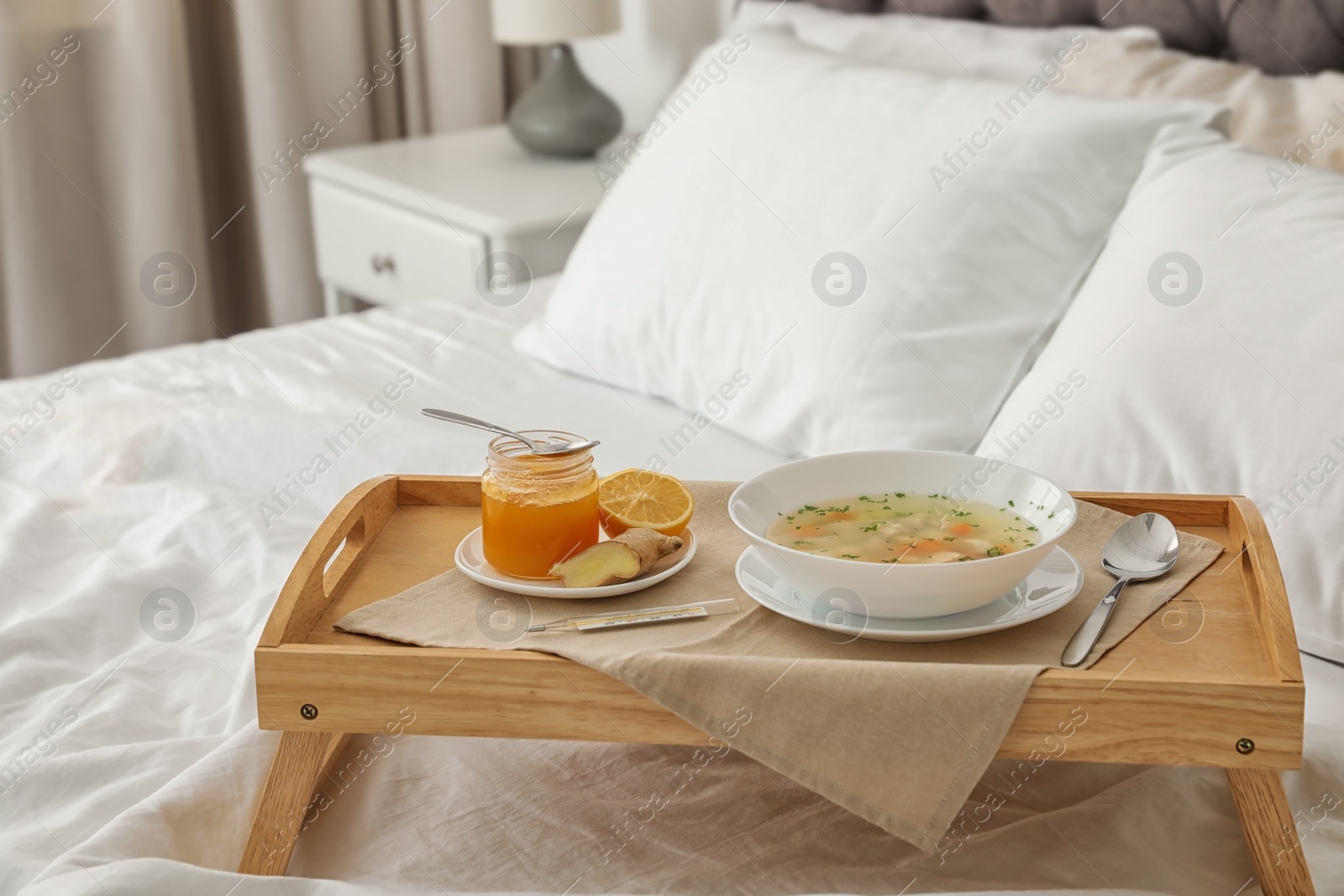 Photo of Tray with bowl of fresh homemade soup to cure flu on bed