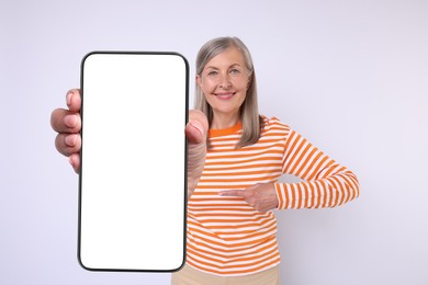 Happy mature woman showing mobile phone with blank screen on white background. Mockup for design