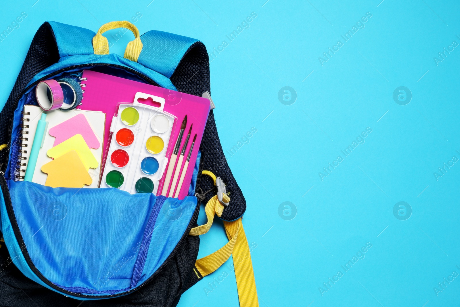 Photo of Backpack with school stationery on light blue background, top view. Space for text