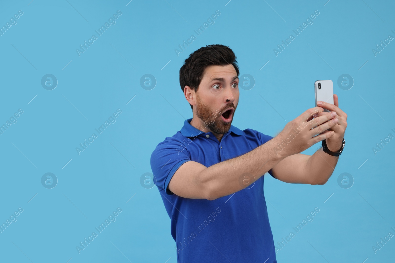 Photo of Surprised man taking selfie with smartphone on light blue background, space for text