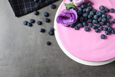 Tasty blueberry cake decorated with flowers on grey table, flat lay. Space for text