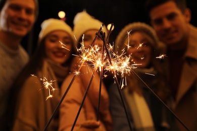 Photo of Grouppeople holding burning sparklers, focus on fireworks