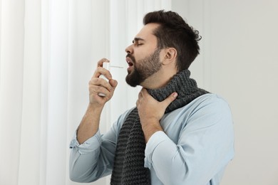 Photo of Young man with scarf using throat spray indoors