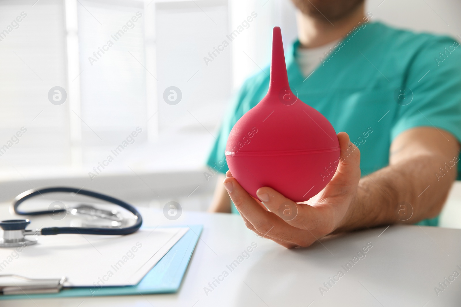 Photo of Doctor holding pink enema at table in hospital, closeup