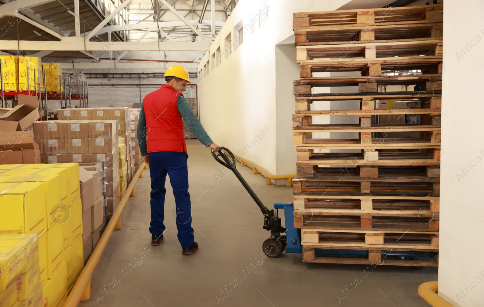 Image of Worker moving wooden pallets with manual forklift in warehouse