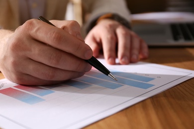 Photo of Businessman working with charts and graphs at table in office, closeup. Investment analysis