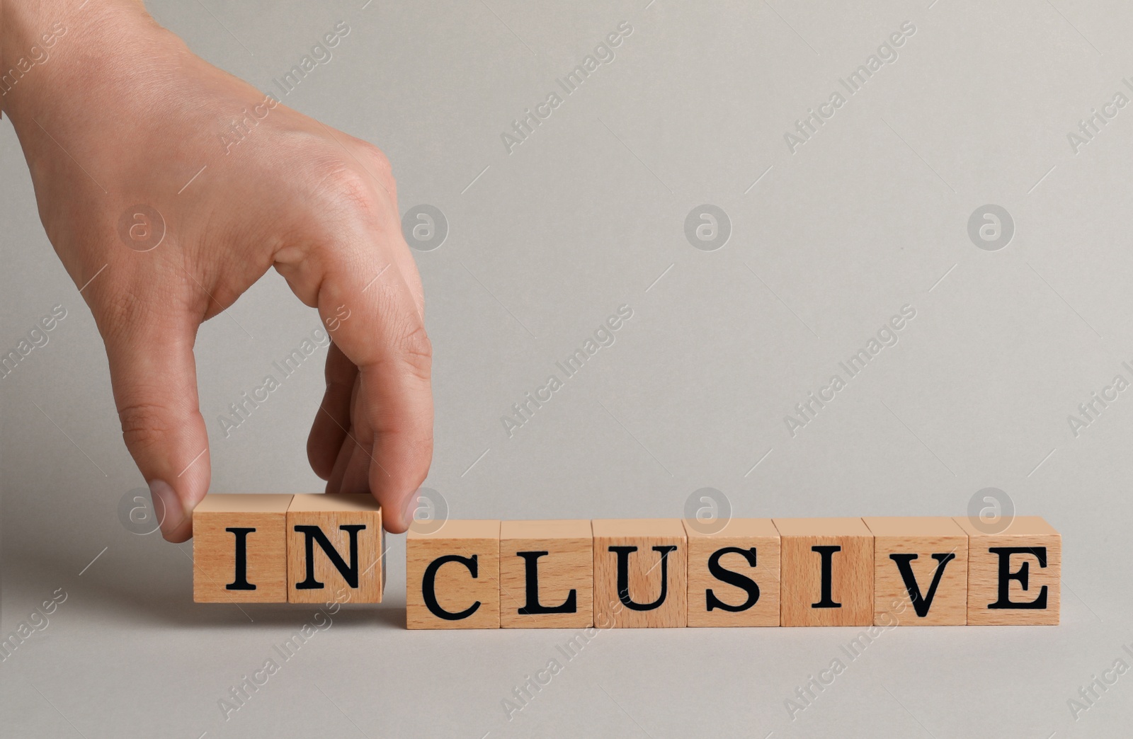 Photo of Woman making word Inclusive with wooden cubes on beige background, closeup. Space for text