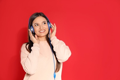 Photo of Attractive young woman enjoying music in headphones on color background. Space for text