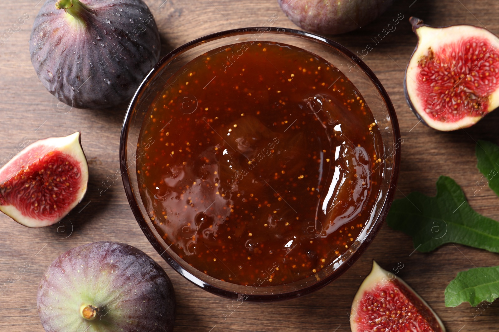 Photo of Glass bowl with tasty sweet jam and fresh figs on wooden table, flat lay