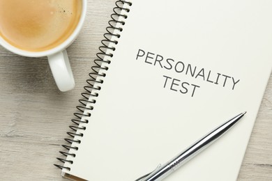 Image of Notebook with text Personality Test, cup of coffee and pen on white wooden table, flat lay