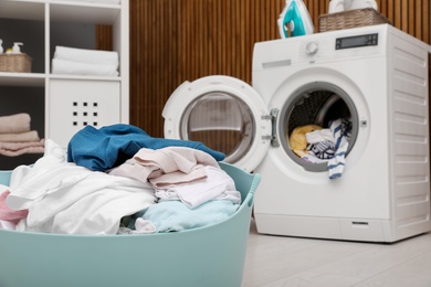 Photo of Laundry basket with clothes and blurred washing machine on background. Space for text