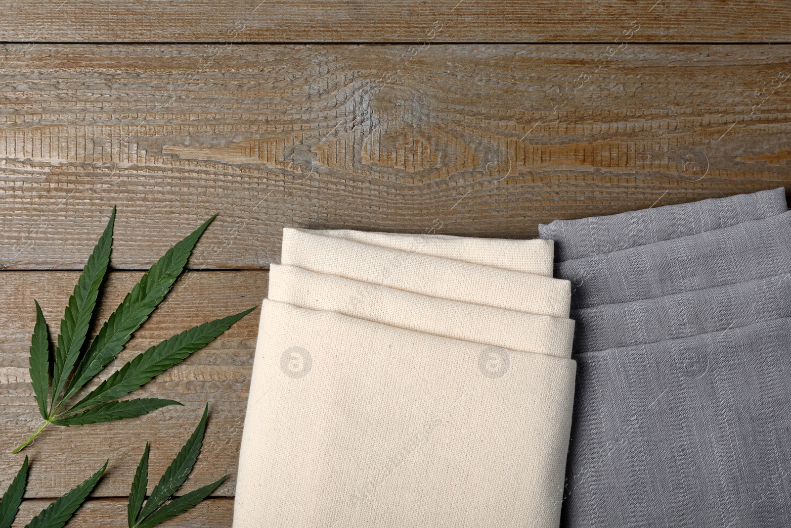 Photo of Hemp cloths and green leaves on wooden table, flat lay. Space for text