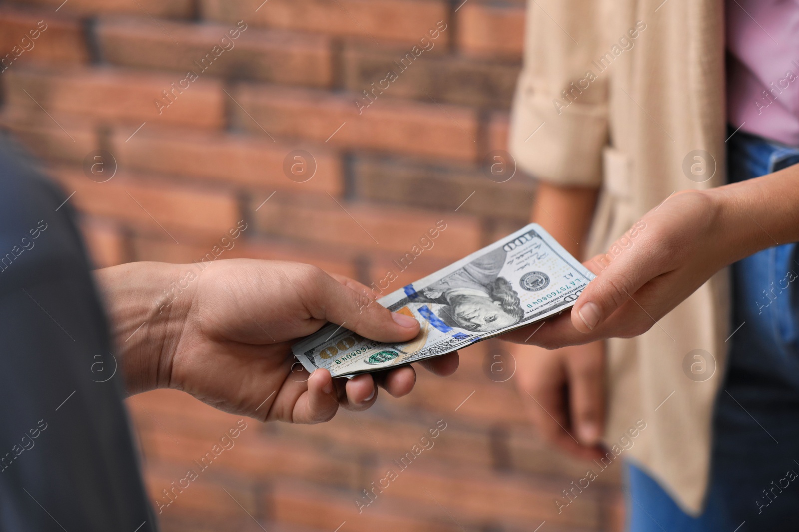 Photo of Man giving woman American money near brick wall, closeup