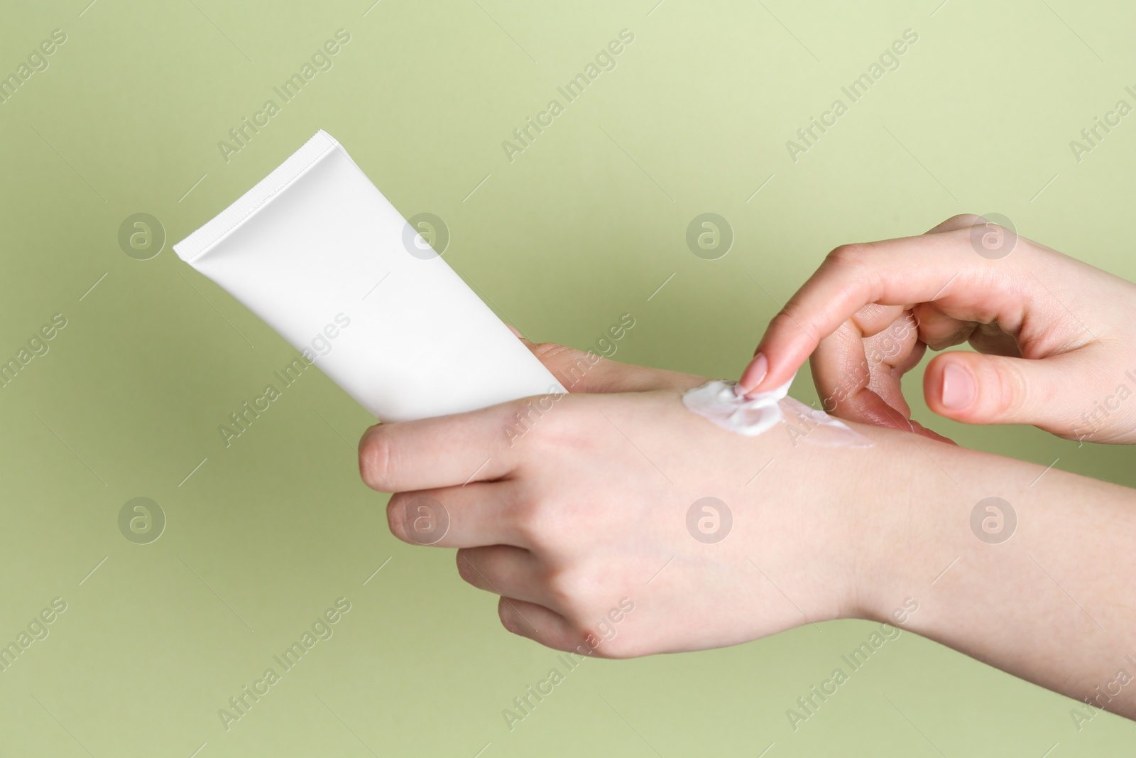 Photo of Woman with tube applying cream on her hand against green background, closeup