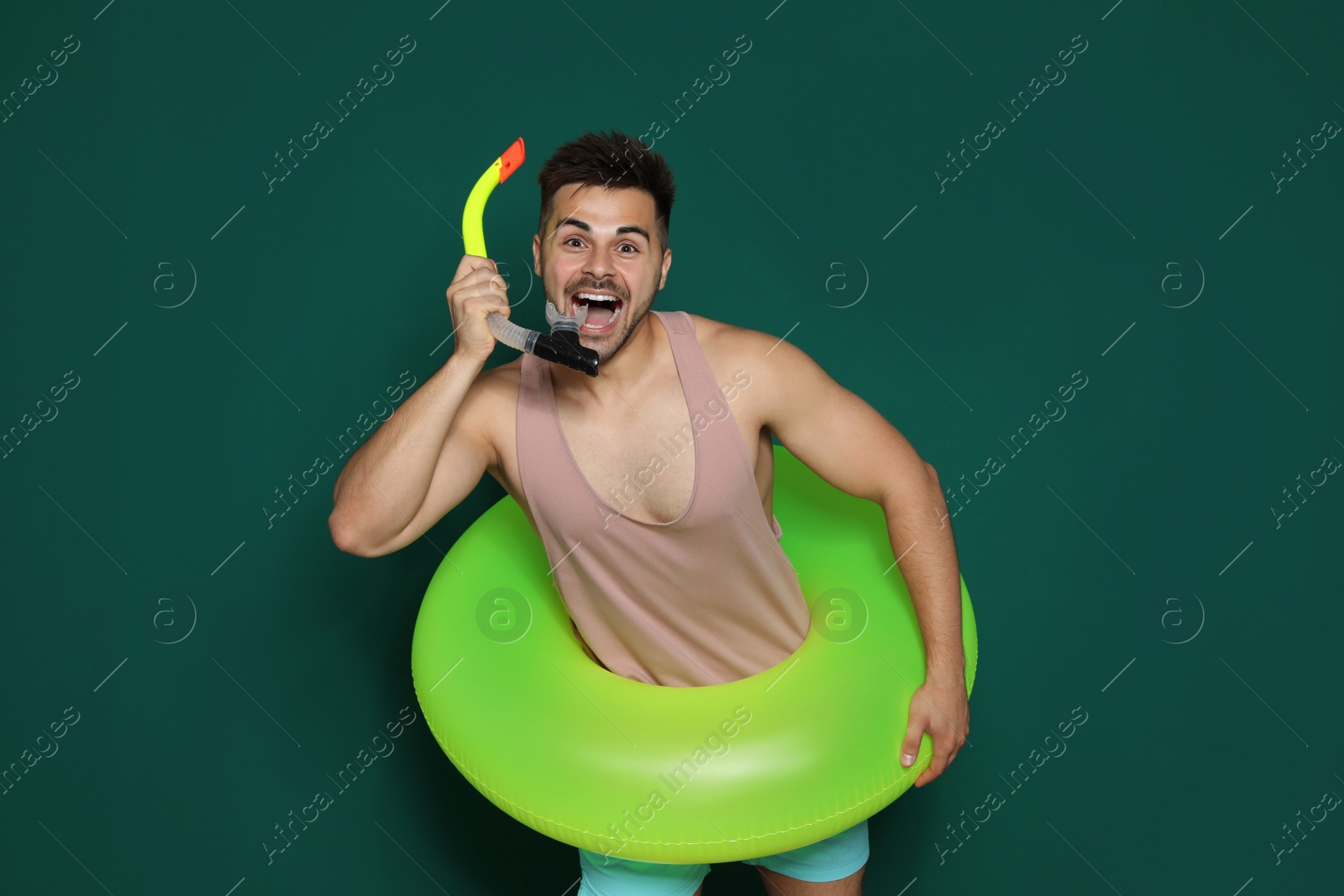 Photo of Funny young man with bright inflatable ring on dark green background