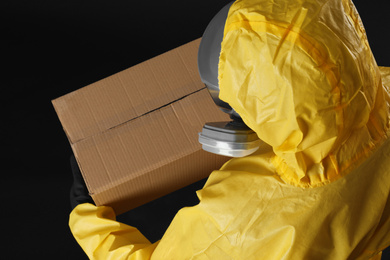 Photo of Man wearing chemical protective suit with cardboard box on black background, above view. Prevention of virus spread