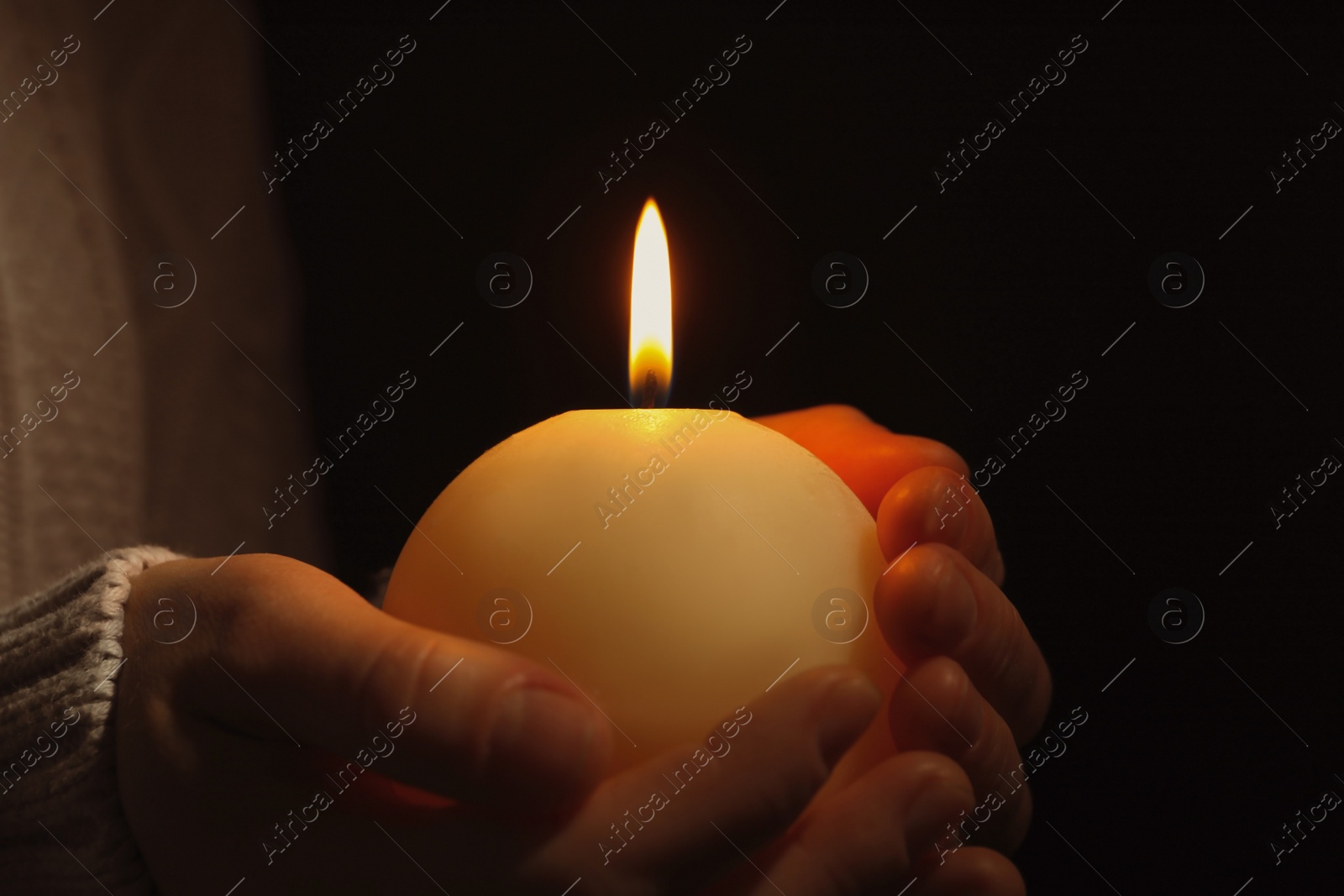 Photo of Young person holding burning candle in darkness, closeup