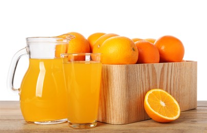 Photo of Fresh oranges in crate and juice on wooden table against white background