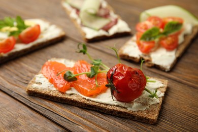 Photo of Fresh rye crispbread with salmon, cream cheese and grilled tomato on wooden table, closeup