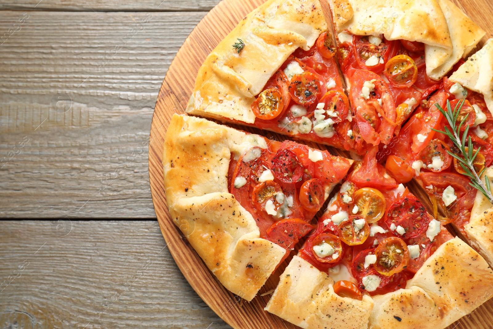 Photo of Tasty galette with tomato, rosemary and cheese (Caprese galette) on wooden table, top view. Space for text