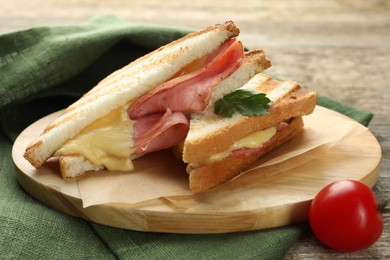 Photo of Tasty sandwiches with ham, parsley, melted cheese and tomato on wooden table, closeup