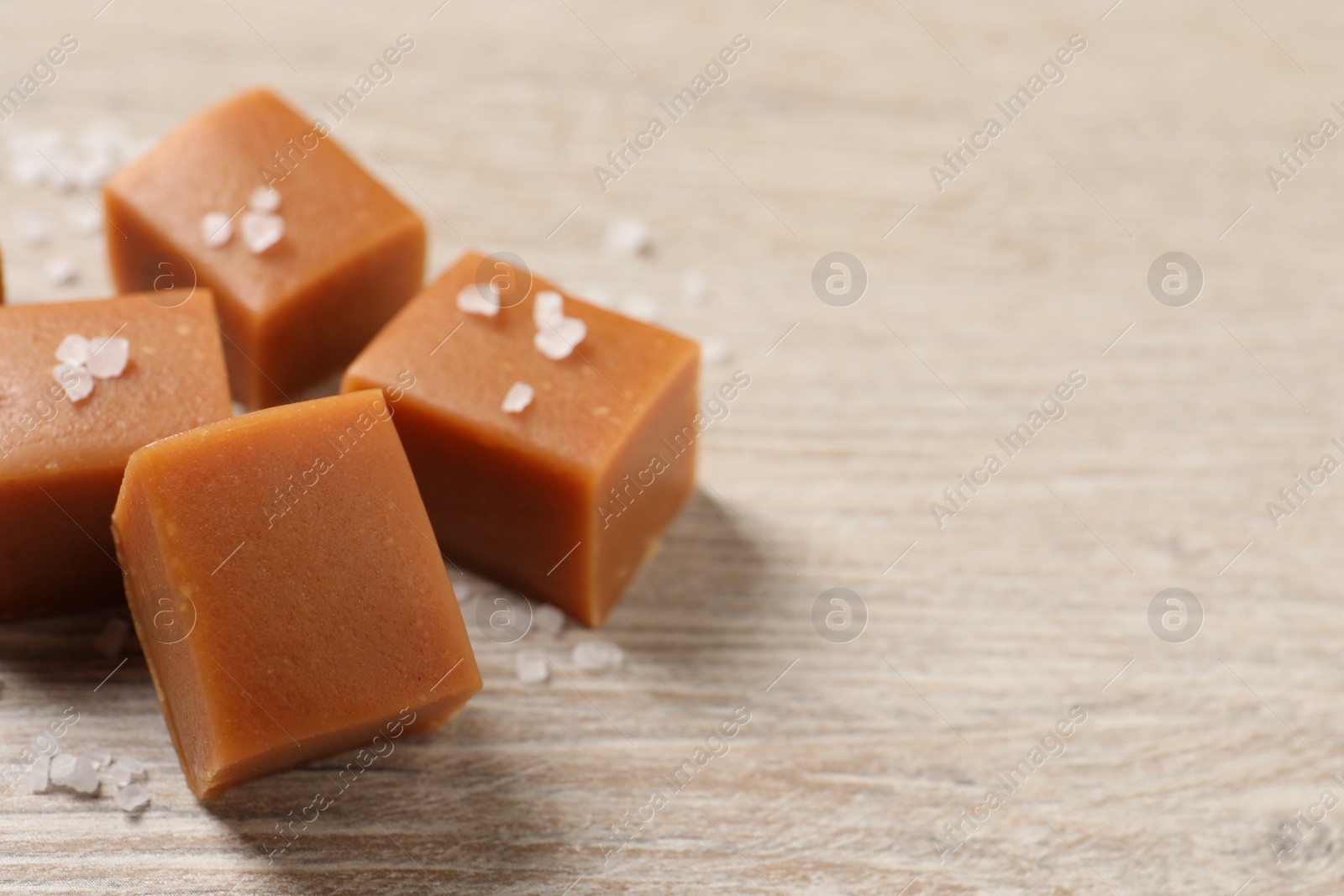 Photo of Tasty caramel candies and sea salt on light wooden table, closeup. Space for text