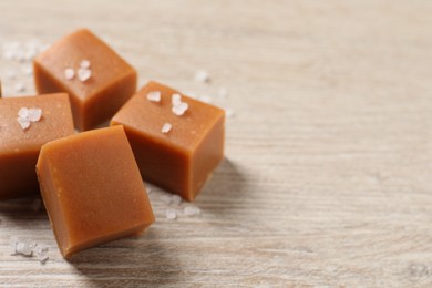 Tasty caramel candies and sea salt on light wooden table, closeup. Space for text