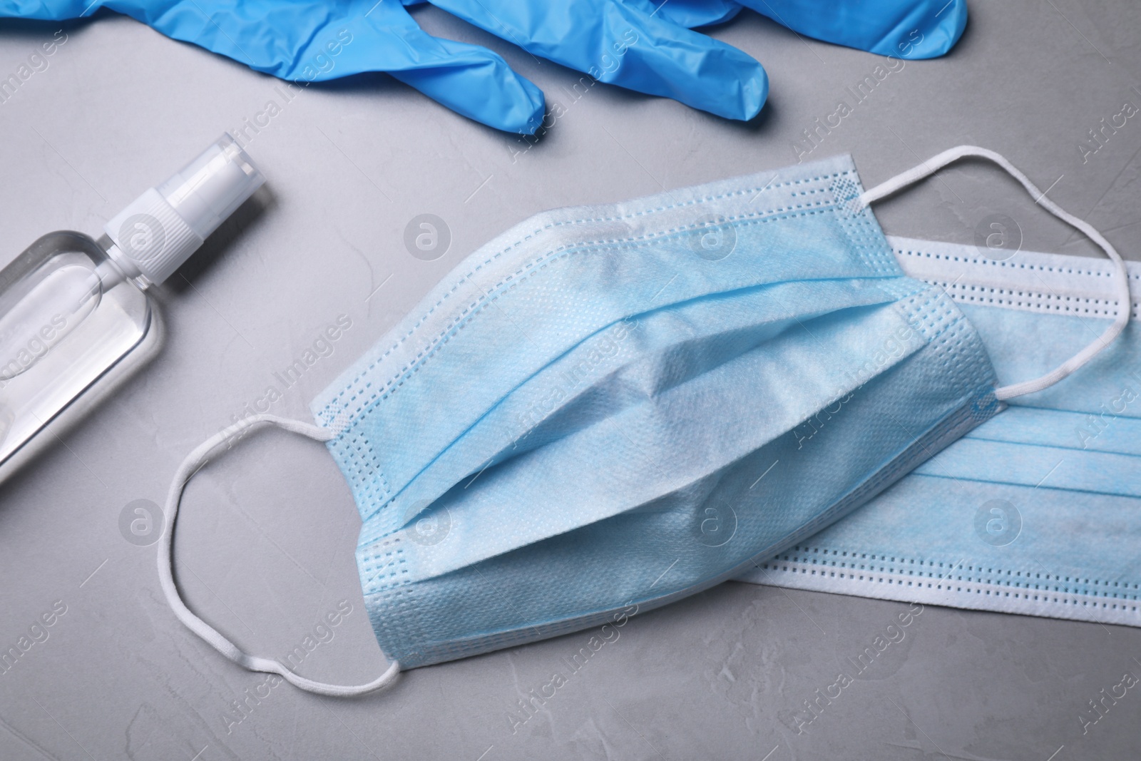 Photo of Protective masks, medical gloves and antiseptic on light grey stone background