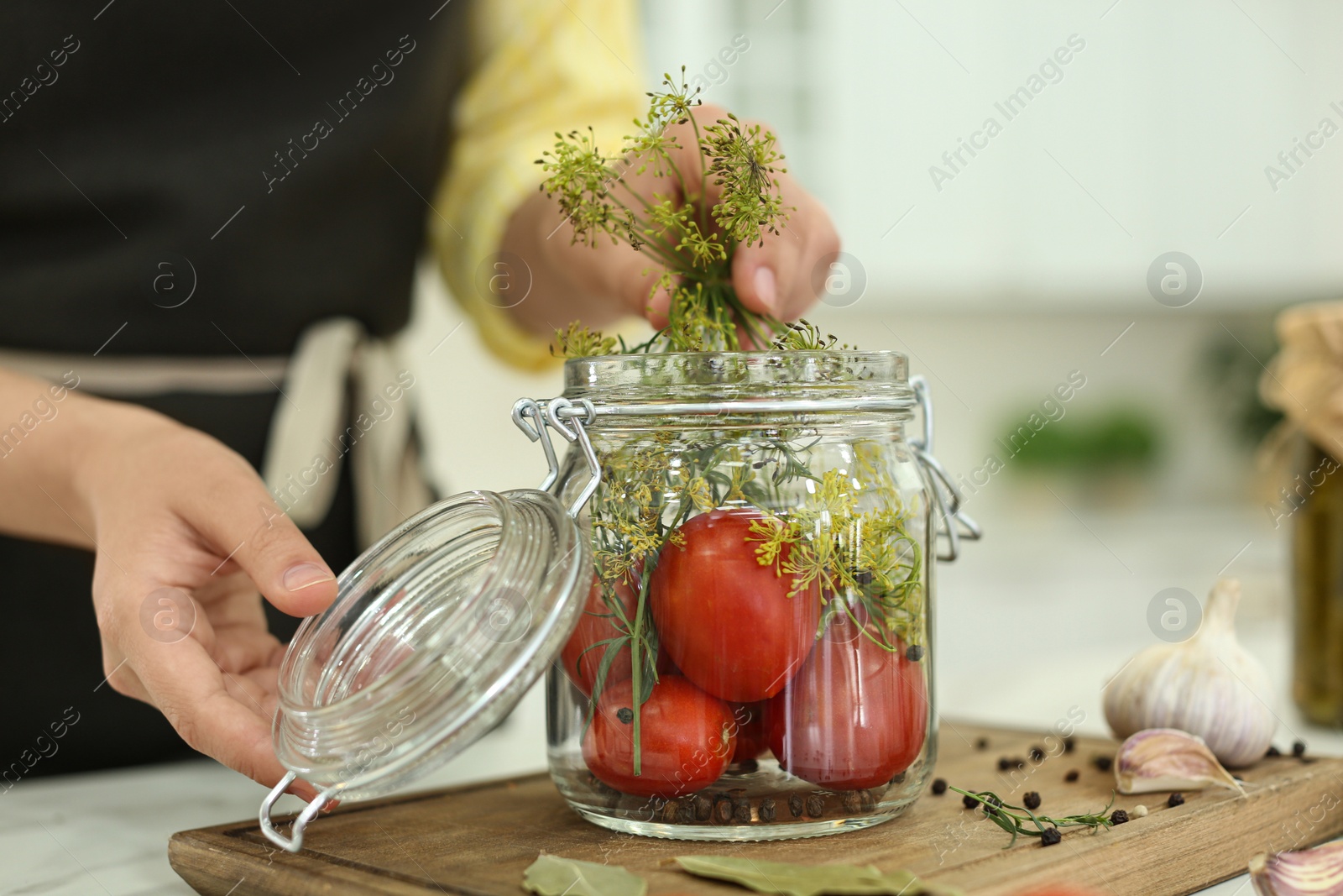 Photo of Woman putting dill into pickling jar at table in kitchen, closeup